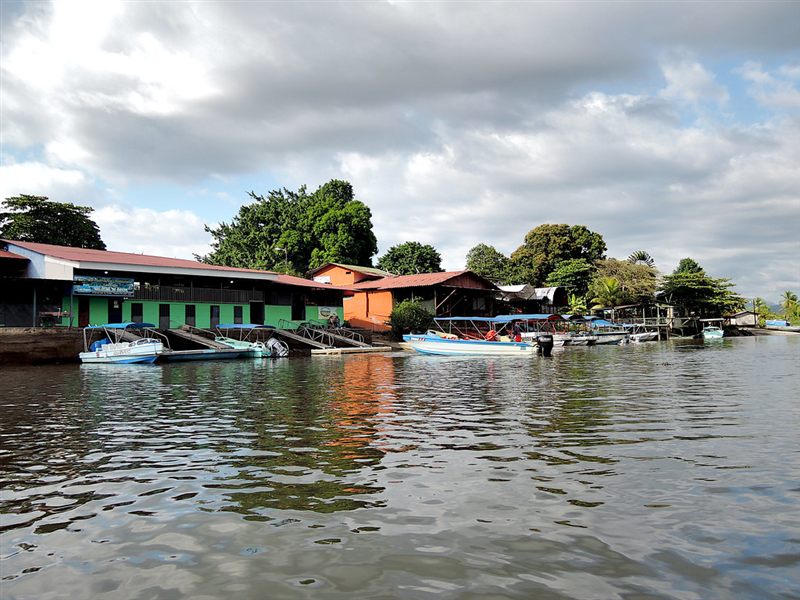 Small passenger boats tied up at a waterside dock below green and orange buildings